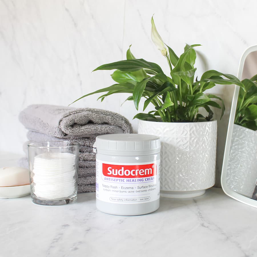 Pot of Sudocrem cream next to plant and towel.